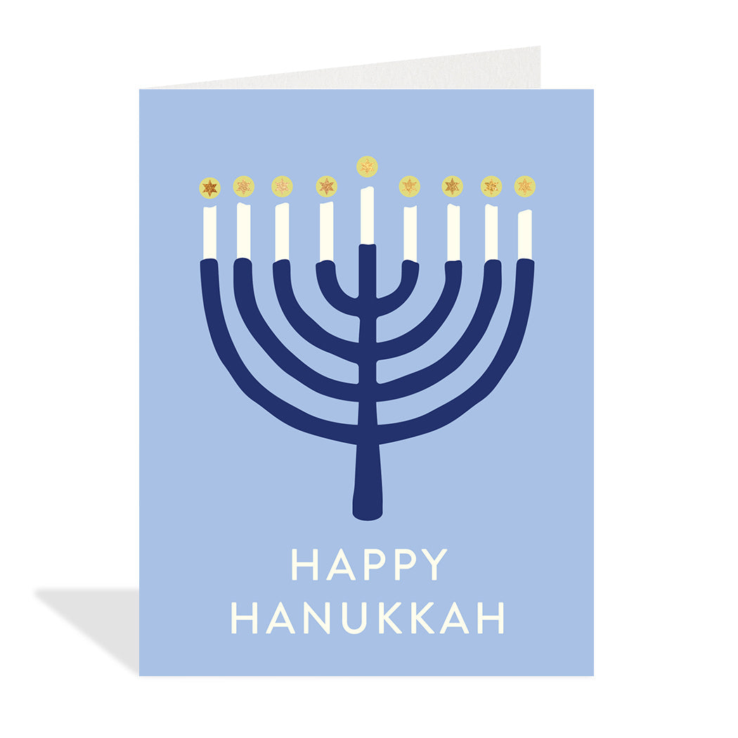 Greeting card designed by Halfpenny Postage. A simple illustration of a lit navy blue Menorah on a light blue background with the sentiment Happy Hanukkah in gold foil at the bottom.