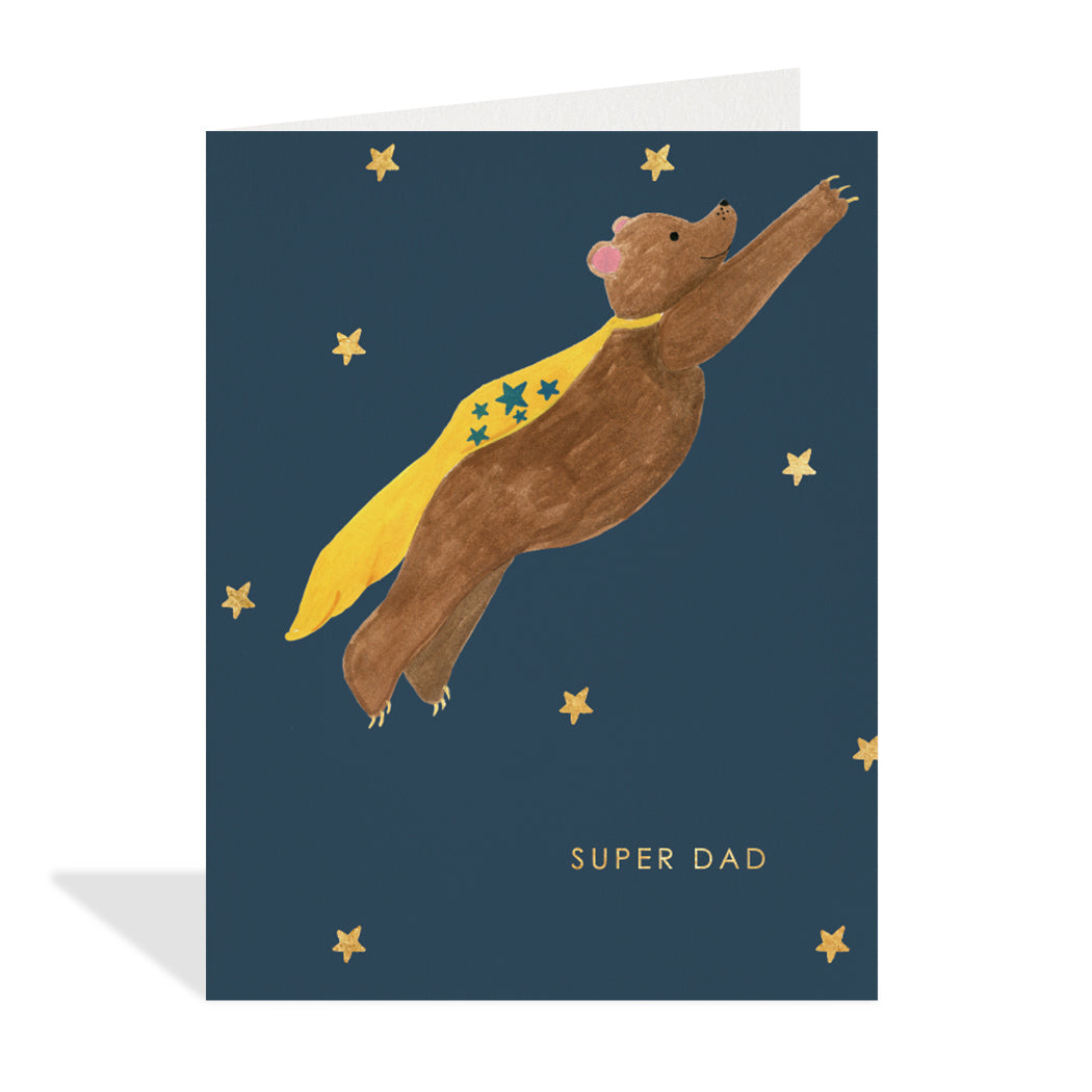 Greeting card design by Hutch Cassidy. A cute illustration of a brown bear wearing a yellow cape, flying through the stars in the night sky with a gold foil sentiment that reads "super dad".
