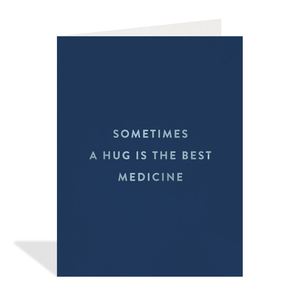 Greeting card designed by Halfpenny Postage. A simple design with a silver foil quote that reads, "sometimes a hug is the best medicine" on a navy blue background. 
