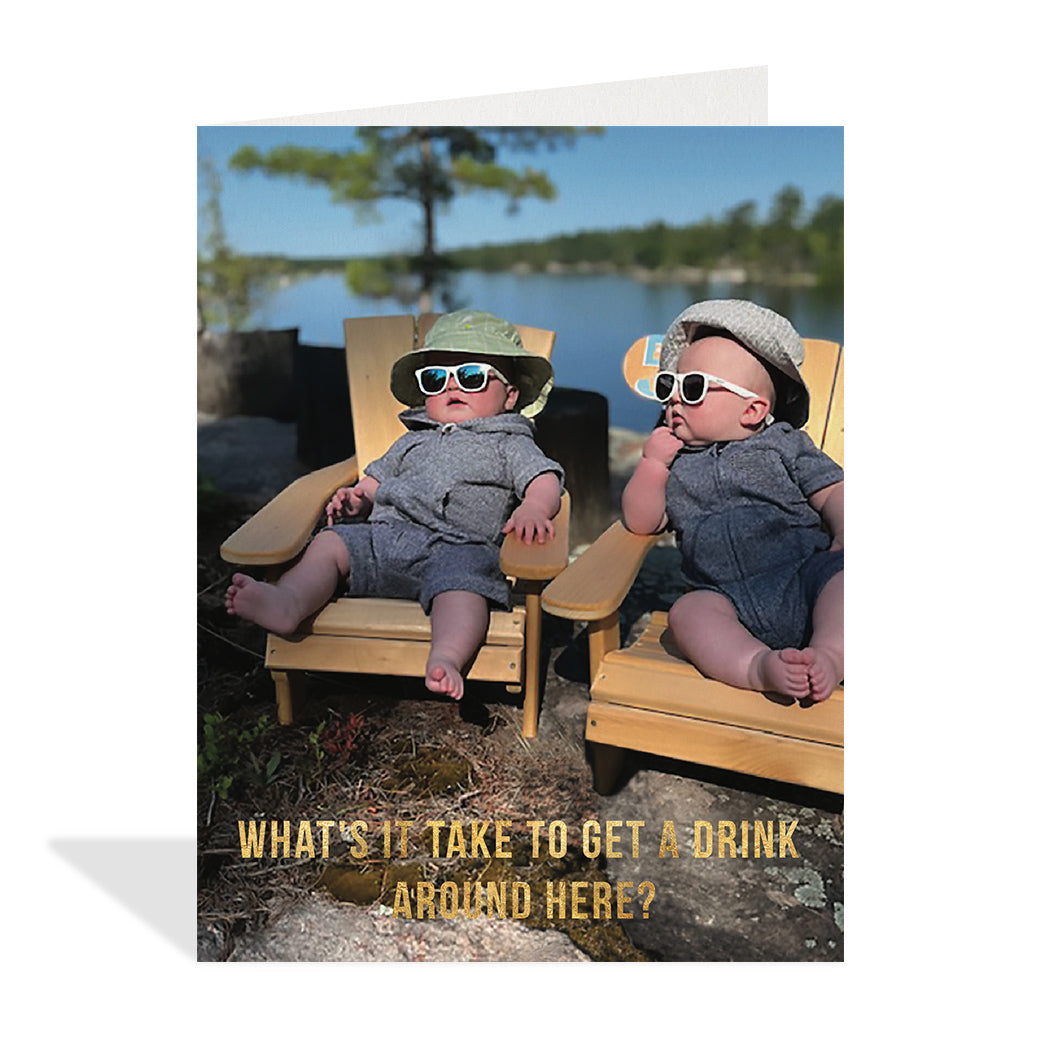 Funny photographic card of two babies waiting and sitting in chairs wearing sunglasses and hats. Gold foil typography that reads "What's it take to get a drink around here?".