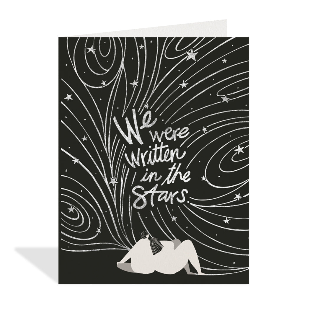 Greeting card design by Hannah Beisang. A charming illustration of a couple sitting and watching the silver foil stars in the night sky with a silver foil sentiment that reads "we were written in the stars".