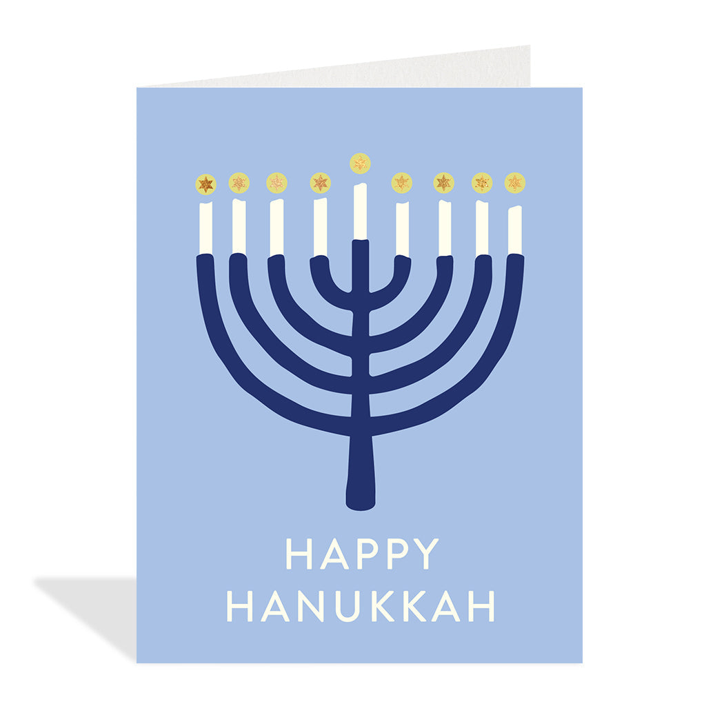Greeting card designed by Halfpenny Postage. A simple illustration of a lit navy blue Menorah on a light blue background with the sentiment Happy Hanukkah in gold foil at the bottom. 